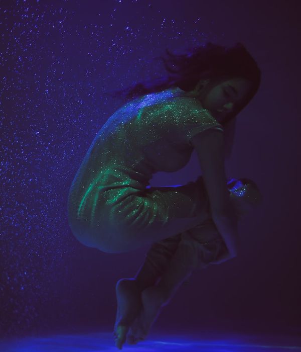 Woman in a calm yoga pose in a dark room with blue light accents.